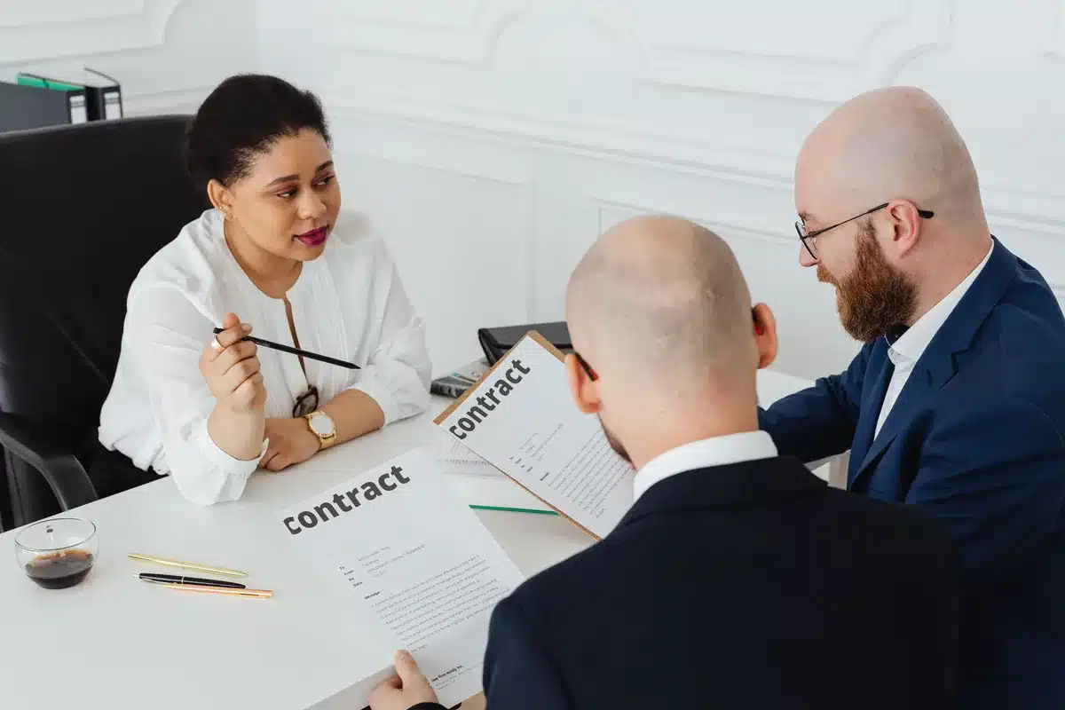 Trois personnes examinent ensemble un contrat papier au-dessus d'une table de bureau.