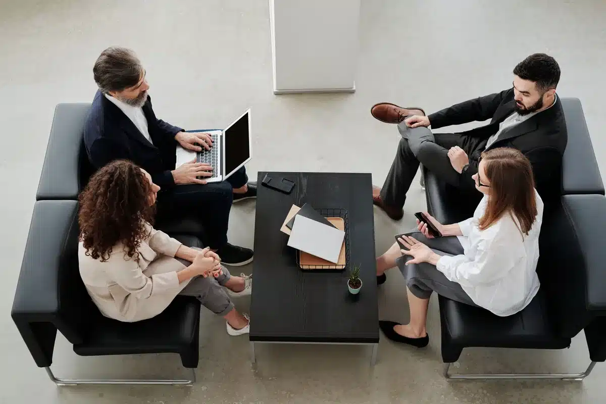 Réunion de travail vue de dessus : plusieurs personnes autour d'une table avec ordinateurs portables et documents.