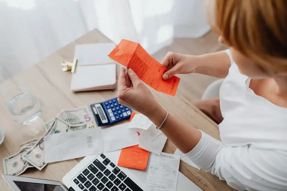 Une personne calcule des dépenses avec une calculatrice et des reçus sur un bureau.