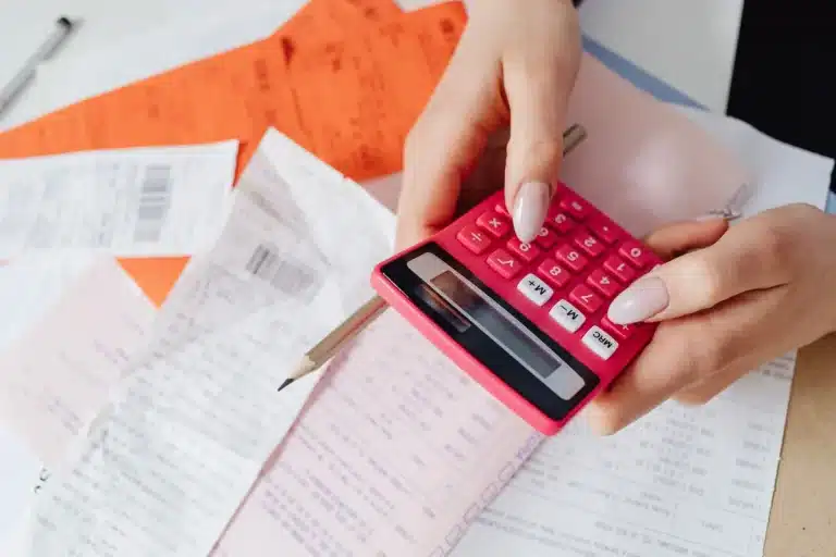 Calculatrice, billets et documents de paie sur un bureau.