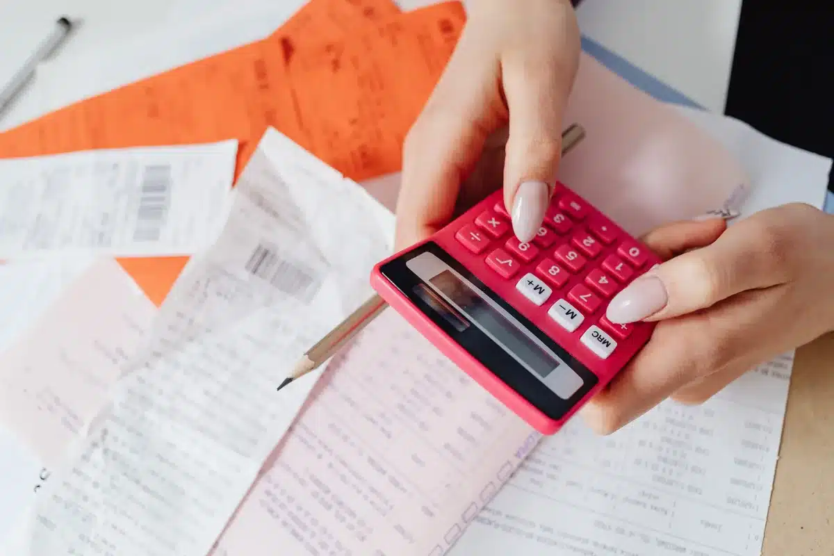 Calculatrice, billets et documents de paie sur un bureau.